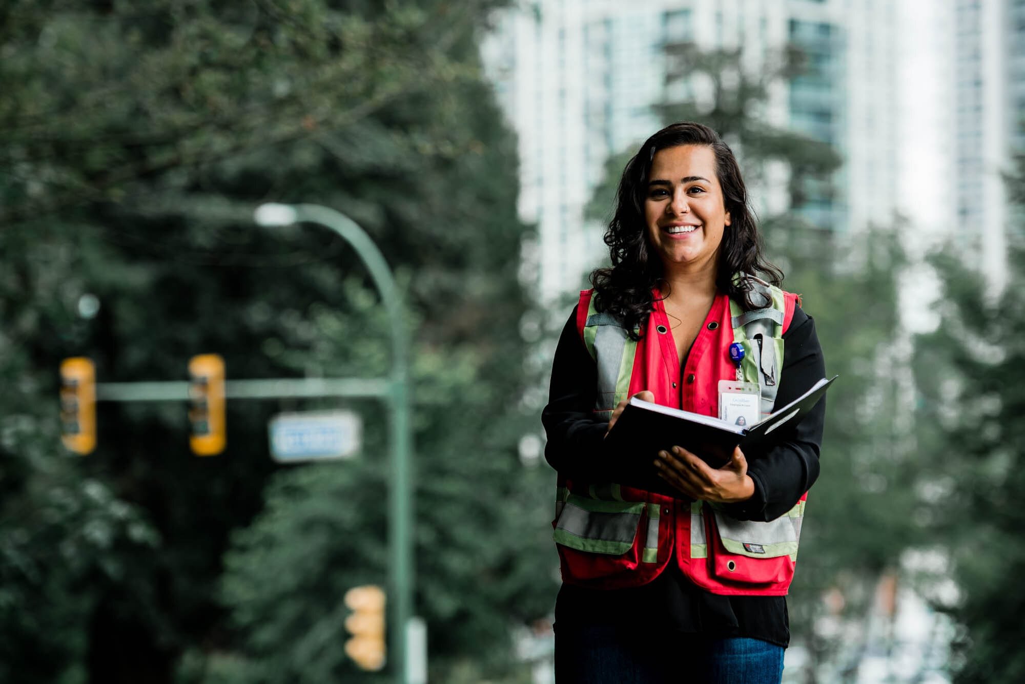 CoquitlamCityHR-3 Smiling woman in safety vest holding notebook outdoors.