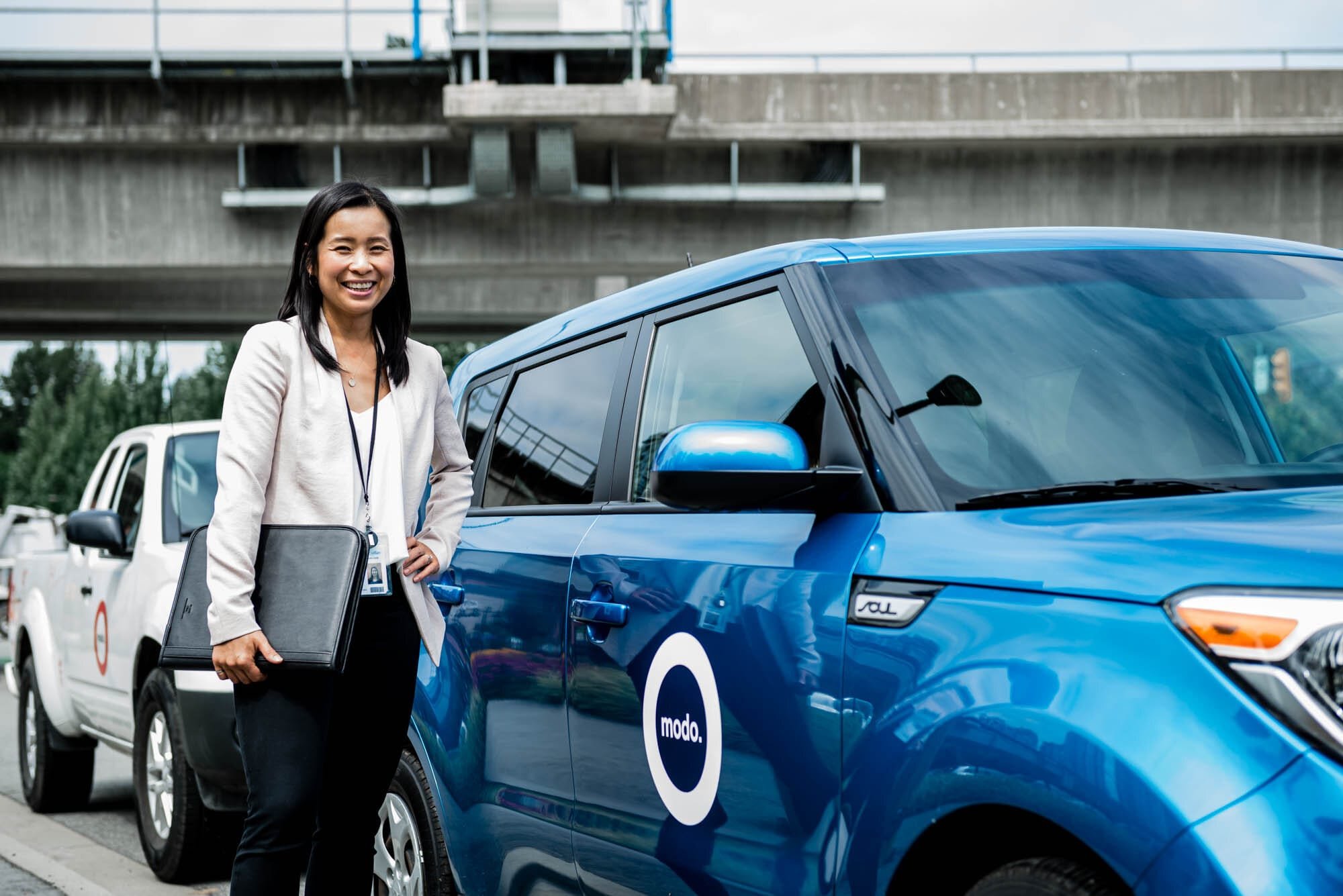 CoquitlamCityHR-7 Woman standing beside blue Modo car.