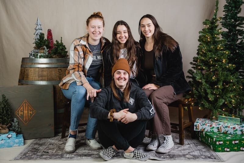 Four people posing with Christmas decorations and gifts.