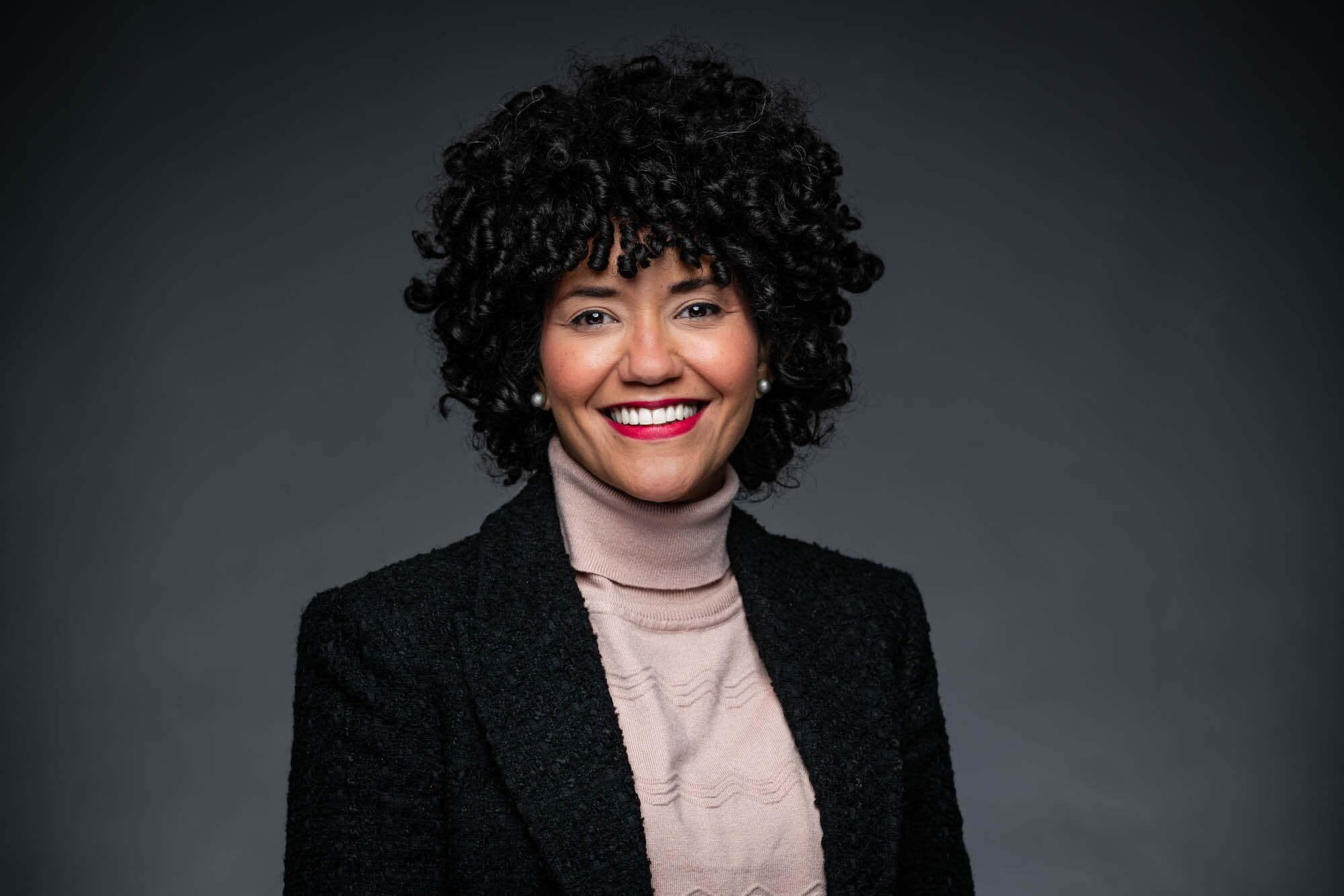 GeaCongress Headshots-10 Smiling person with curly hair and dark blazer
