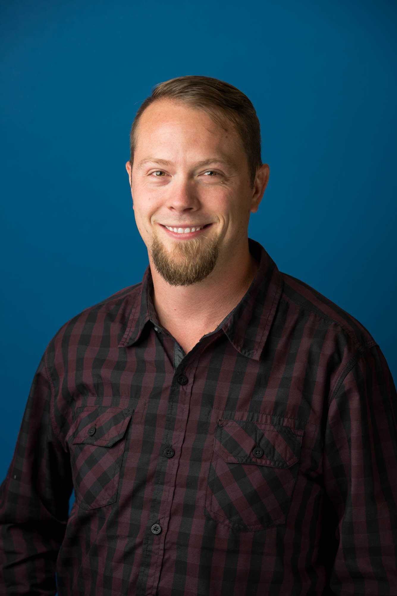 Rose Security Headshots-6 Smiling man in plaid shirt, blue background