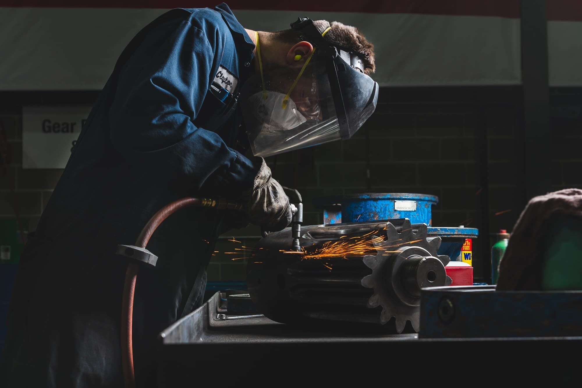 BAP_3682 Technician wearing safety gear grinding metal part.