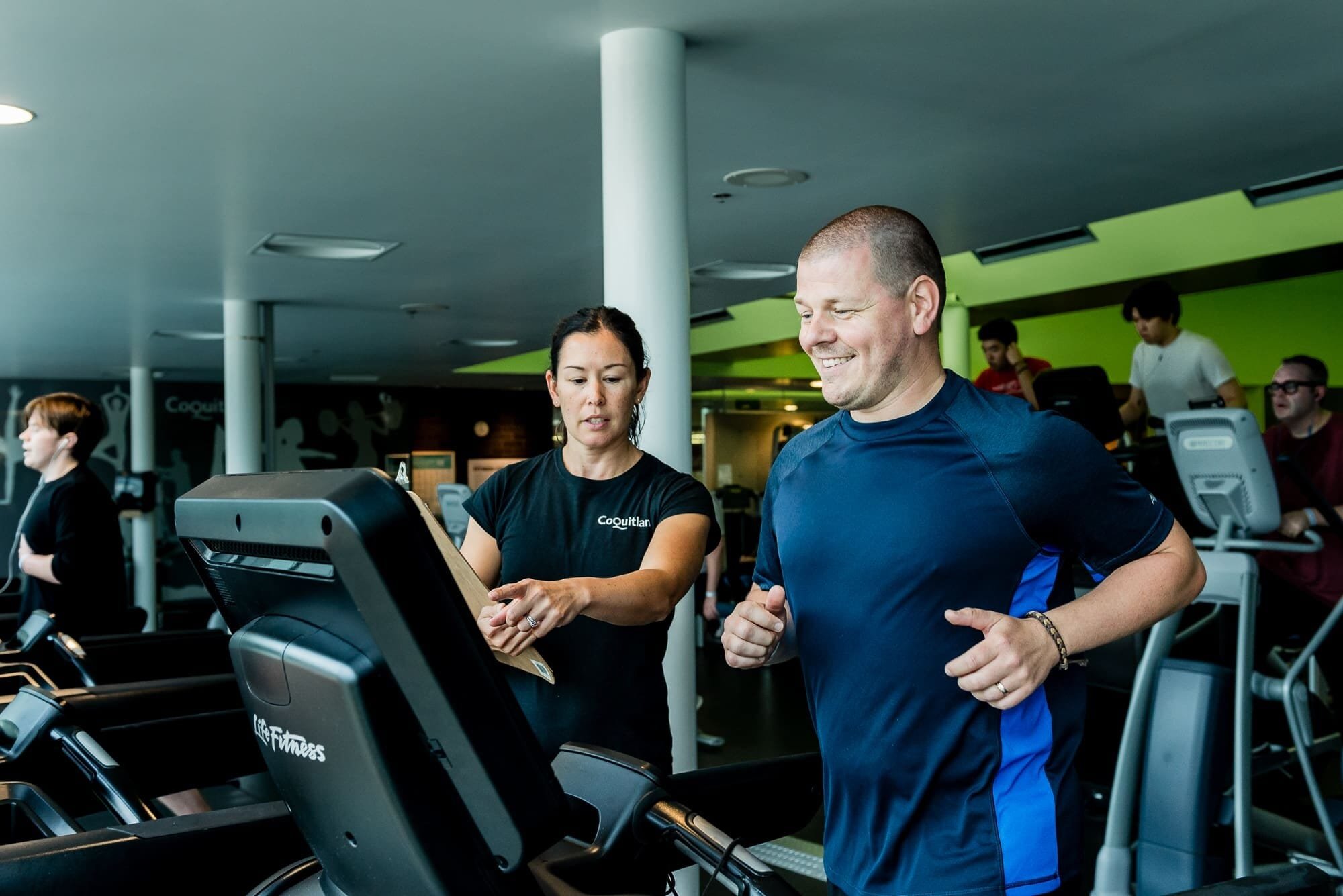 BAP_9078 Trainer assists man jogging on treadmill.
